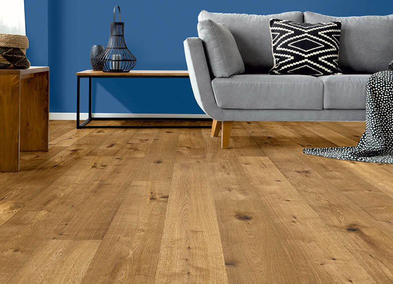 Aktuelle Wohn-Trends: Heller Holzboden. Im Hintergrund ist eine graues Sofa und eine blaue Wand zu sehen.