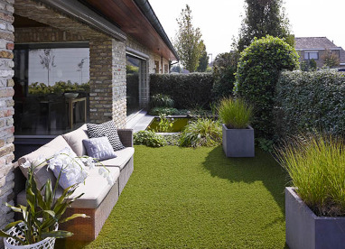 Outdoor-Living: Ein Garten mit stilvollen Outdoor-Möbeln, Kunstrasen und Deko-Kissen.